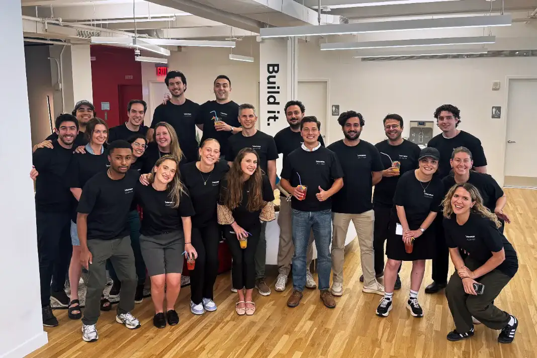 Intenseye team members in matching company t-shirts gathered in the office beside a 'Build it.' pillar